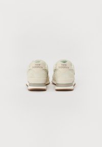 Vaaleanvihreät nubukitennarit, joissa on teksturoitu pinta, pehmustettu nilkkareuna ja beigeet yksityiskohdat. Sivuissa on "new balance" -brändäys kantapäällä.