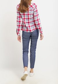 Rutig rosa och vit flanellskjorta med lång ärm och skräddarsydd passform; kombinerad med blåa skinny jeans och vita sneakers.