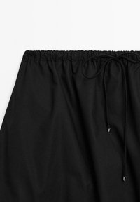 Gonna nera con vita elastica e dettaglio con coulisse. Tessuto liscio. Presenta accenti argentati alle estremità della coulisse.