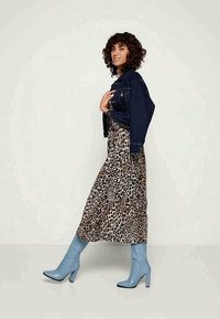 Casaco de ganga sobre um vestido maxi com estampado de leopardo; botas de salto alto em azul claro e texturadas. O conjunto apresenta um design descontraído, mas ajustado.
