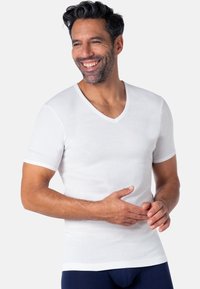 T-shirt blanc en coton à manches courtes avec un col en V, au textile doux et à la coupe ajustée, porté avec un bas bleu marine.
