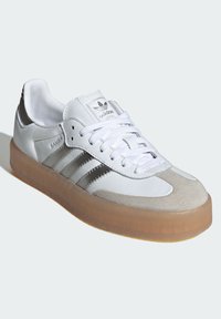 Białe skórzane sneakersy z szarymi zamszowymi akcentami, trzema srebrnymi paskami i przezroczystą gumową podeszwą. Sznurowadła oraz wyściełany kołnierz dopełniają całość.