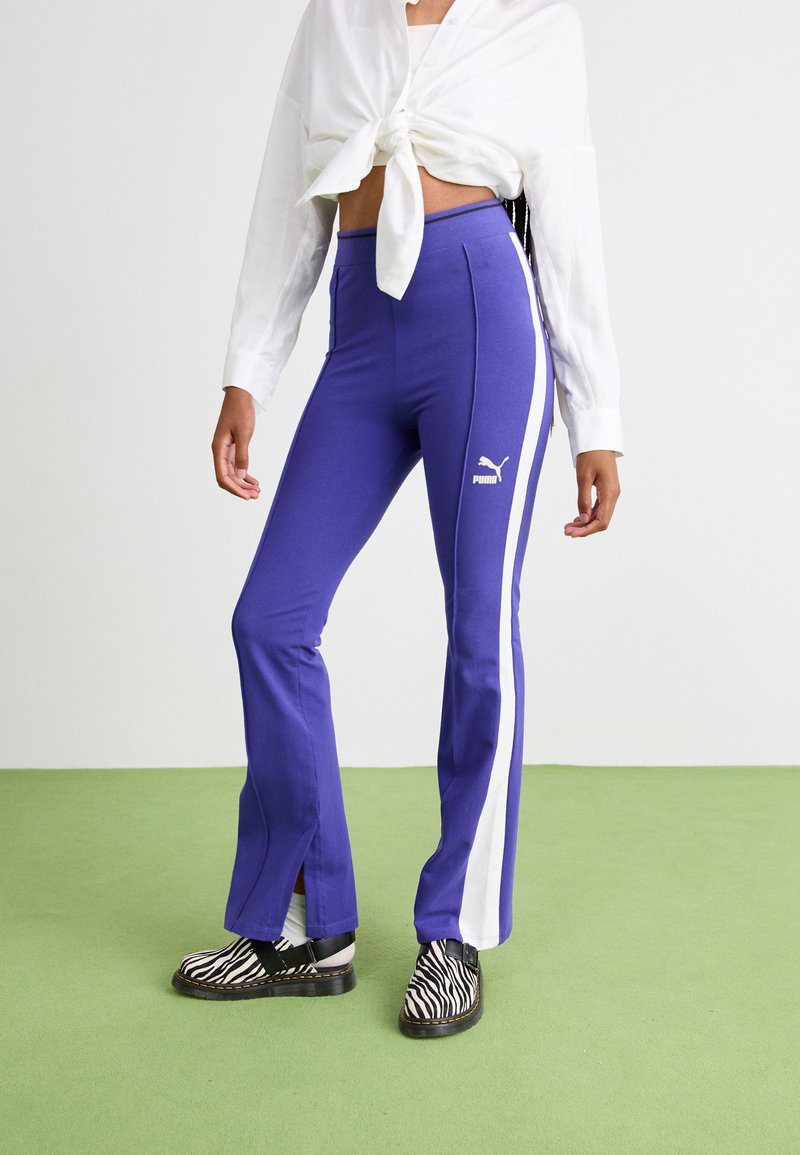 Lila utsvängda byxor med vita sidostripes, tillverkade av mjukt tyg, med en Puma-logotyp. Kombinerade med svart och vit zebramönstrade skor.