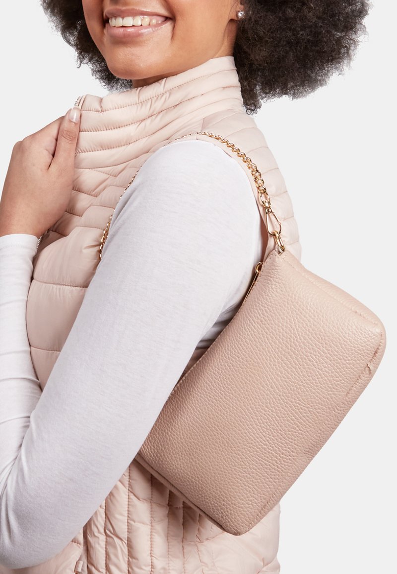 Borsa a tracolla in pelle rosa con texture a ciottoli, forma rettangolare e tracolla a catena, posizionata sulla spalla di una persona contro un gilet chiaro.