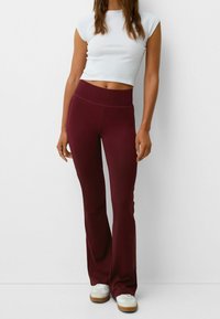 Bordové rozšířené kalhoty s vysokým pasem, vyrobené z elastického materiálu. V kombinaci s přiléhavým bílým krátkým topem s krátkým rukávem a bílými botami.