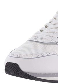 Zapatilla blanca con parte superior de malla texturizada, acentos grises y cordones redondos. Cuenta con una suela de goma con patrones de relieve para agarre.