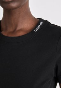 Černé bavlněné tričko s kulatým výstřihem, s vyšitým logem Calvin Klein v bílé barvě na límci. Hladká textura, slim fit design.