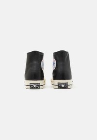 Sneakers alte nere con tomaia in pelle liscia, suola in gomma e rifiniture bianche. Presentano una patch rotonda con il logo su ciascun tallone, design classico.