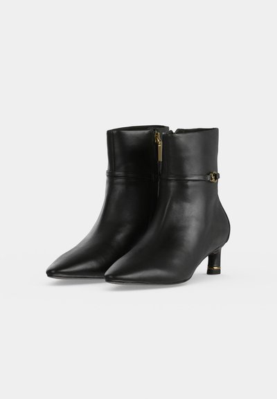 Par de botines de cuero negro con punteras puntiagudas, tacones bajos, cremalleras laterales y pequeños detalles de hebillas doradas.