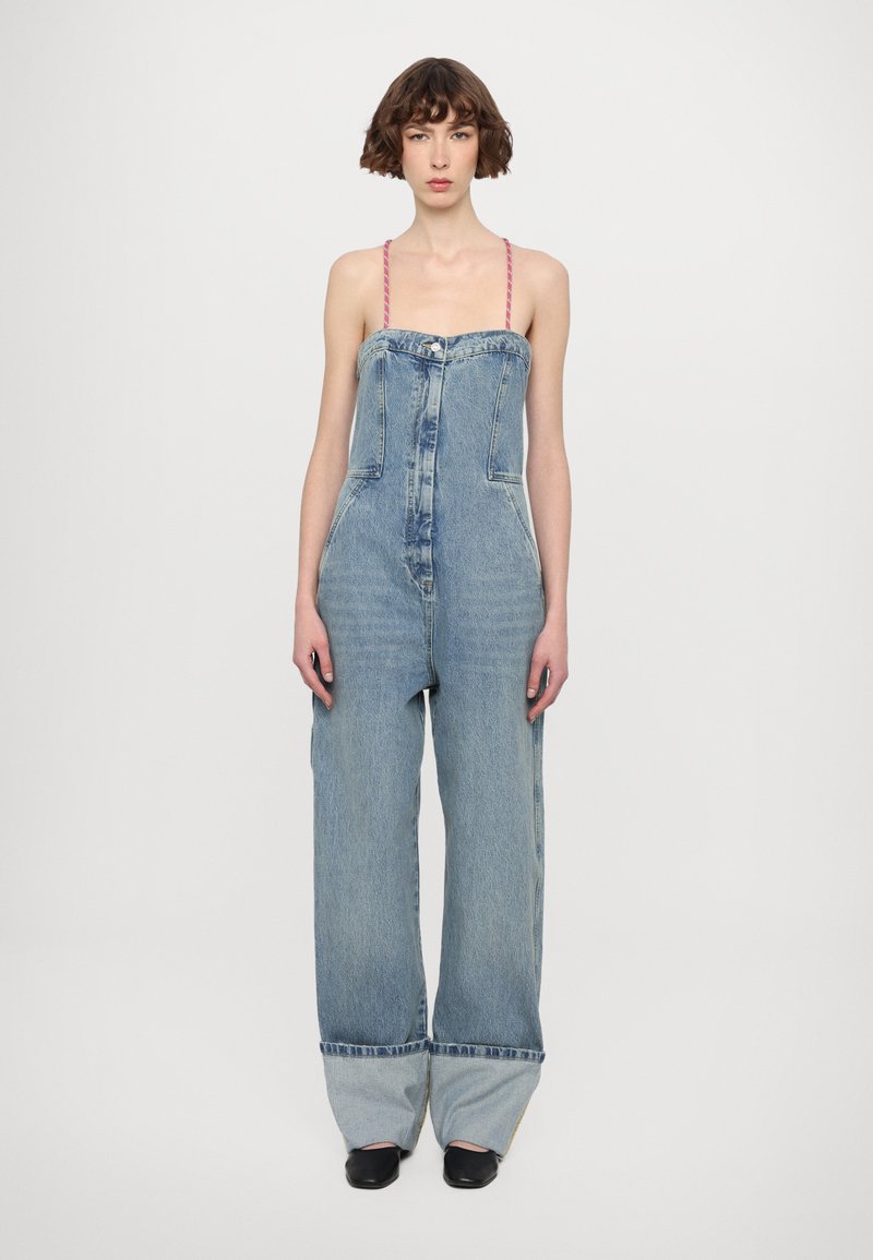 Denim kombinezon s širokimi hlačnicami, svetlo modre barve, sprednjim gumbom za zapiranje in tankimi rožnatimi naramnicami. Umetno obrabljeno blago na dnu.