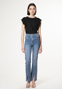 Top nero con maniche a volant, abbinato a jeans blu a vita alta con orlo a spacco, caratterizzati da un lavaggio chiaro e dettagli di cucitura sul davanti.