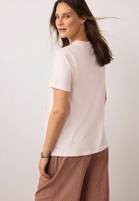 Šviesiai rožinė trumpomis rankovėmis marškinėliai iš minkštos medžiagos, su apvaliu iškirptu kaklu ir laisvo silueto, derinami su rudomis languotomis plačiomis kelnėmis.