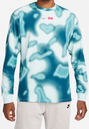 Homme portant un t-shirt à manches longues tie-dye turquoise et blanc avec un logo Nike rose, associé à un short Nike beige clair.