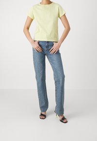 Ljust gult bomullströja med korta ärmar, kombinerat med blå raka jeans. Svarta klacksandaler med gula accenter på klackarna.