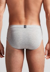 Graue Baumwollunterhosen mit einer weichen Textur, ausgestattet mit einem breiten Bund und einem kleinen Markenlabel auf der Rückseite, in einem klassischen Schnitt.