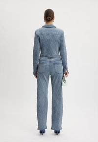 Conjunto de denim azul claro que incluye una chaqueta acolchada y pantalones de cintura alta. La tela tiene un patrón de diamante texturizado. Acentuado con tacones azules.