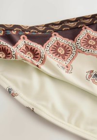 Mönstrad tyg i kräm, brunt och rosa med blommotiv; slät textur; avskurna kanter; hänger något och avslöjar inre foder.