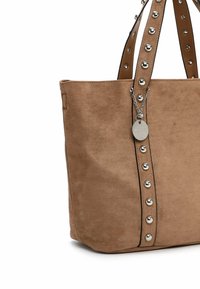 Sac en suede marron avec des clous en argent sur les côtés, deux poignées et un accent en chaîne attaché à une étiquette décorative.