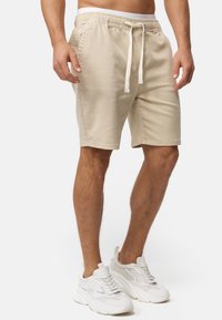 Beige bomuldsshorts med elastisk talje og justerbar snor. Har sidelommer og et lige snit. Sammen med hvide sneakers.
