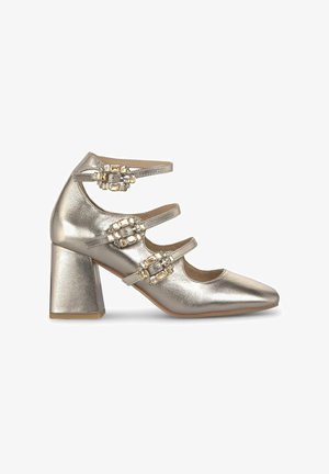 Zapato de tacón alto plateado metálico con punta afilada, que presenta tres correas ajustables y acentos joya en las correas. Diseño de tacón cuadrado.