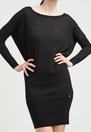 Schwarzes Strickkleid mit langen Ärmeln, weitem Boot-Ausschnitt, figurbetonter Silhouette und kleinem gesticktem Detail nahe dem Saum. Strukturierter Strickstoff.