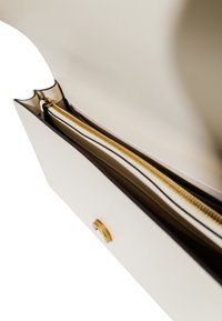 Bolso estructurado blanco con una cremallera dorada, parcialmente abierto para revelar un forro interior beige y compartimentos separados.
