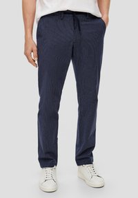 Navy-blaue gestreifte Hose mit einem Kordelzugbund, schlanke Passform und glatter Textur, kombiniert mit weißen Sneakers.