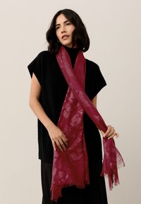 Burgundy scarf with a textured leaf pattern, soft fabric, fringed edges, draped around the neck, paired with a black top.