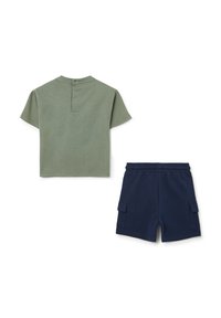 Camiseta de algodón verde con mangas cortas y cierre de botón en la parte posterior, combinada con pantalones cortos de algodón azul marino con bolsillos laterales.