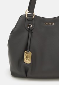 Borsa a mano in pelle nera con una finitura texture, dotata di accessori in tonalità oro e di un'etichetta. La parte superiore ha un design arrotondato e una sola tracolla.