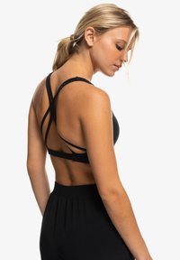 Sostén deportivo negro con un diseño de espalda entrecruzada, hecho de una tela elástica, con tirantes ajustables y una textura suave.