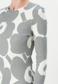 Ribbet langermet topp i grått og hvitt, med et blomster mønster med store, abstrakte former og rund hals.