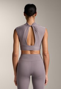Cropped top viola chiaro con schiena annodata e design aperto, abbinato a leggings a vita alta dello stesso colore, entrambi realizzati in tessuto morbido.