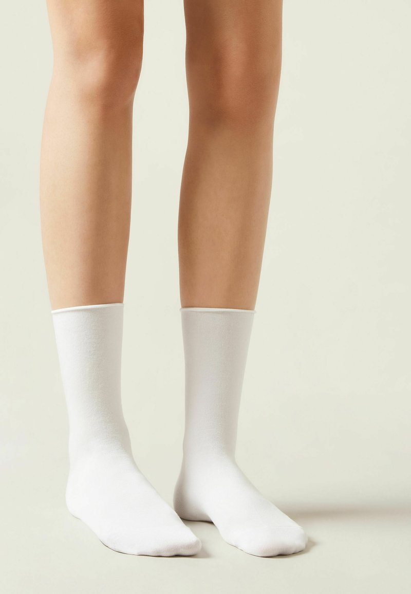 Hvide bomuldscrew-sokker med en glat tekstur, tætsiddende design og ribbet top, vist på ben imod en lys baggrund.