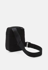 Borsa nera in nylon a forma quadrata, con un pannello in rete testurizzato, tracolla regolabile e chiusura con zip nella parte superiore.