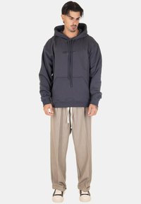 Felpa grigia scura con tasca a kangaroo e coulisse. Abbinata a pantaloni beige chiaro plissettati e sneakers nere con suola bianca.
