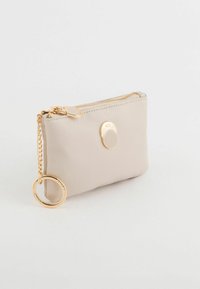 Portefeuille en cuir beige clair avec fermeture éclair, garnitures dorées et attache pour porte-clés. Texture lisse avec peu de détails.