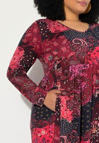 Pitkähihainen mekko, jossa on sekoitus paisley- ja kukkakuoseja punaisen, vaaleanpunaisen ja laivastonsinisen sävyissä. Mekossa on rento istuvuus ja taskut.