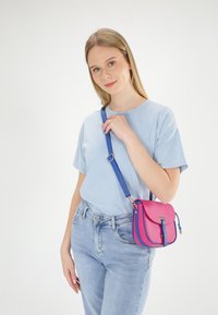 Mała torebka crossbody w różowo-niebieskiej skórze o strukturalnym kształcie i przednim klapce. Regulowany pasek, gładka tekstura i metalowe okucia.