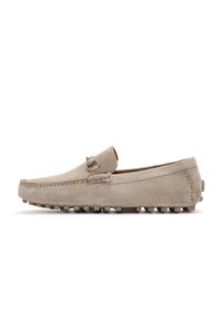 Mocasines de ante beige con un acabado suave, costuras decorativas y suelas de goma con tachuelas para mayor tracción. Presenta un sutil acento metálico.
