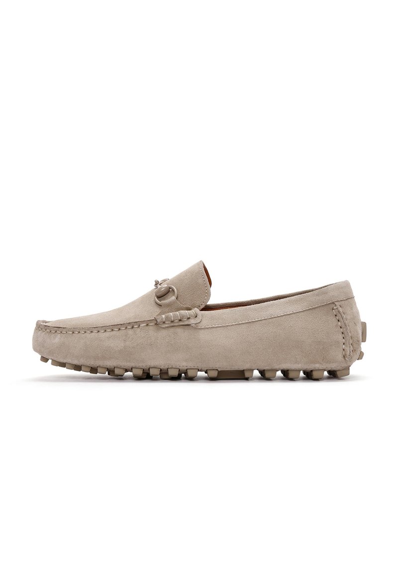 Mocasines de ante beige con un acabado suave, costuras decorativas y suelas de goma con tachuelas para mayor tracción. Presenta un sutil acento metálico.