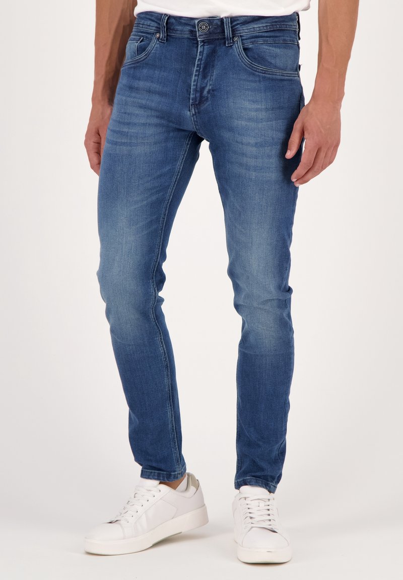 Blå slim-fit jeans av denim med en blekt look, med fem fickor och knappstängning. Matchas med vita sneakers.