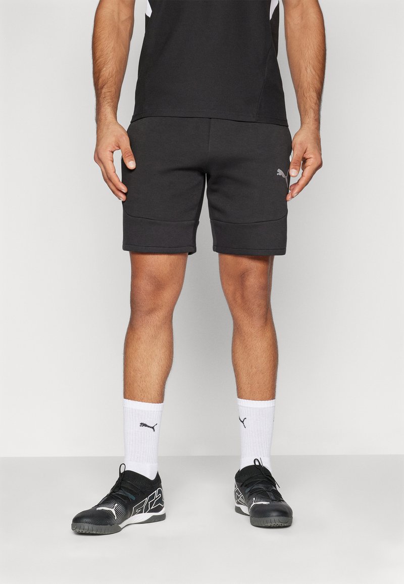 Svarte treningse shorts med sidelommer, en tettsittende design og en myk tekstur. Kombinert med svarte sko og hvite sokker med logoer.