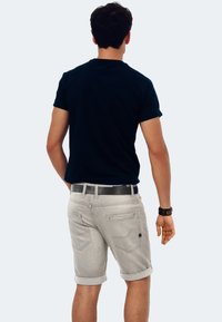 Marineblaues T-Shirt mit kurzen Ärmeln, kombiniert mit hellgrauen Jeansshorts. Die Shorts haben umgeschlagene Säume und Gesäßtaschen. Ein schwarzer Gürtel und eine Uhr sind sichtbar.