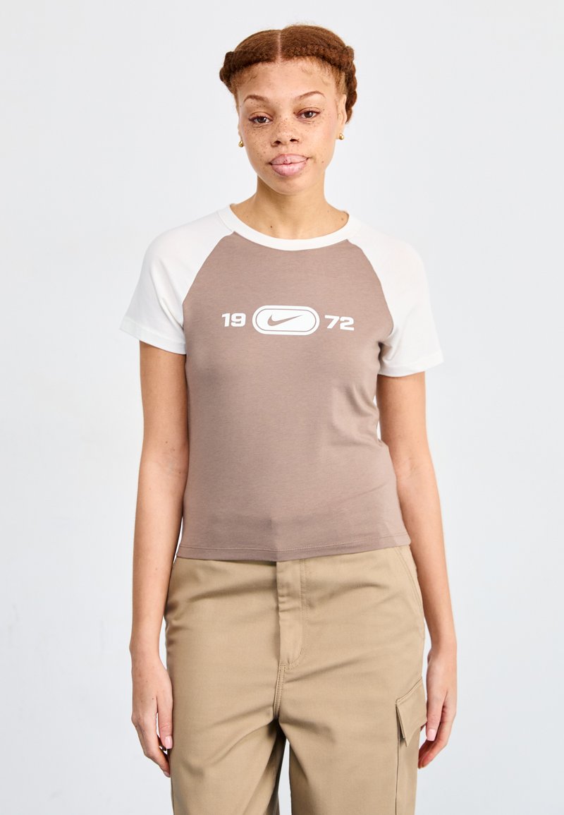 Hnědé a bílé tričko s krátkým rukávem a kulatým výstřihem, se středovým logo Nike a čísly "1972" pod ním.