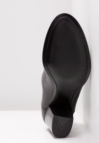 Zapato de cuero negro con suela texturizada, tacón angular y parte superior suave. Cuenta con un diseño minimalista y una marca sutil.