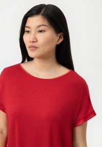 Röd kortärmad topp med rund halsringning. Slät textur och avslappnad passform, med uppvikt ärmslut för extra detaljer.