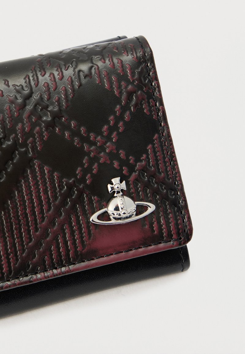 Close-up of black and dark red textured wallet corner featuring a small shiny silver orb logo with a ring and cross on top.