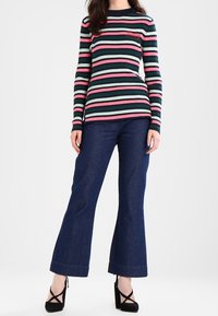 Długi rękaw żebrowany top w poziome paski w kolorze granatowym, różowym i miętowym, zestawiony z rozszerzanymi ciemnymi dżinsami i czarnymi szpilkami.