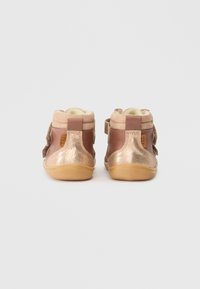 Atgalinė rago vaizdo apžvalga, rudos ir rožinės aukso spalvos batukai vaikams su Velcro diržais ir minkšta pūkinė pamušalu baltoje fone.